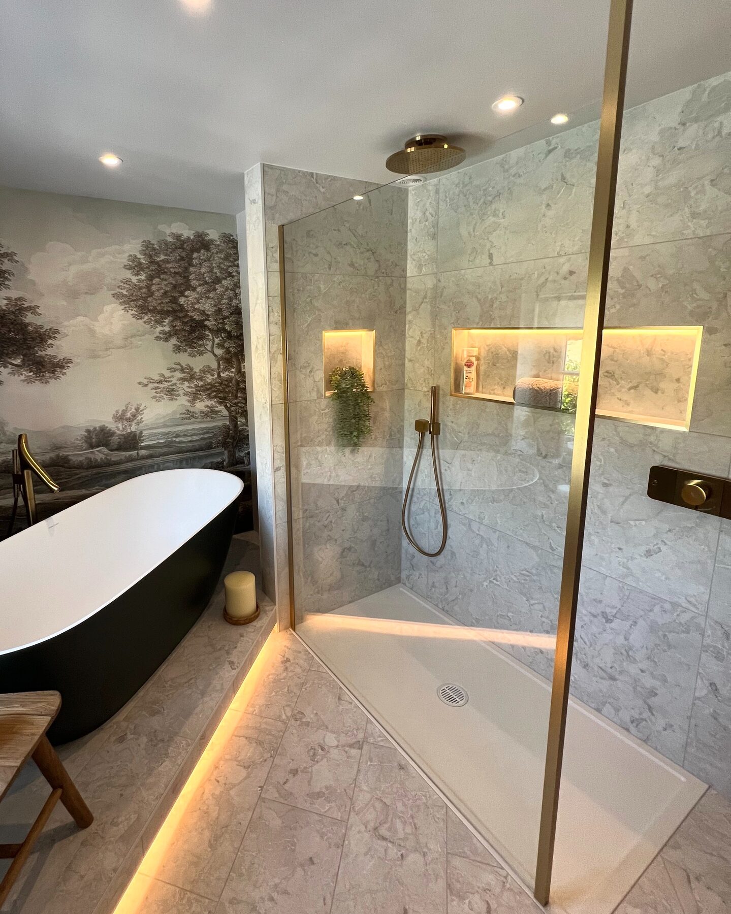 Bath and walk-in shower display with stone-effect tiles and lit niches